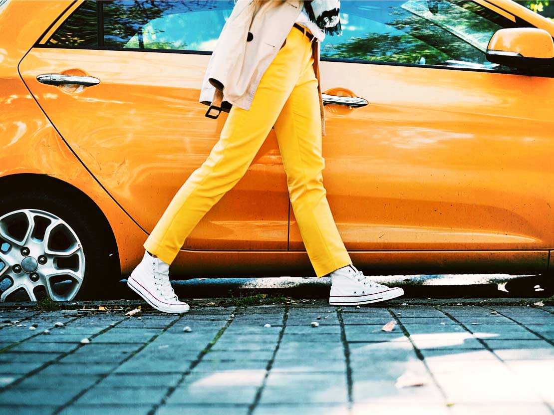 Kvinna i gula byxor gåendes förbi gul bil