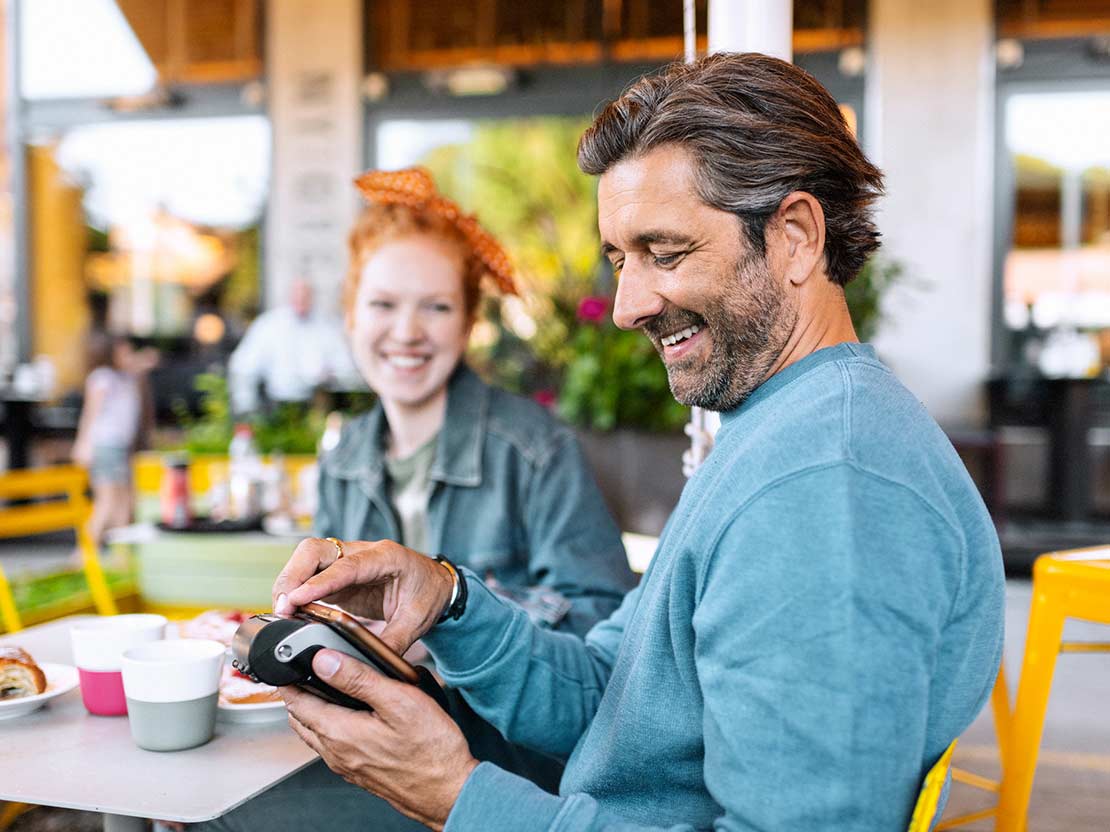 Man i blå tröja betalar med smartphone till kortterminal på café