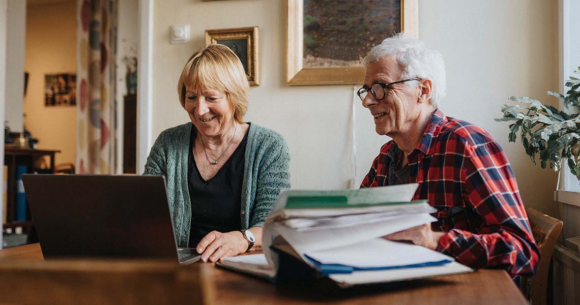 Äldre kvinna och man använder laptop och ler