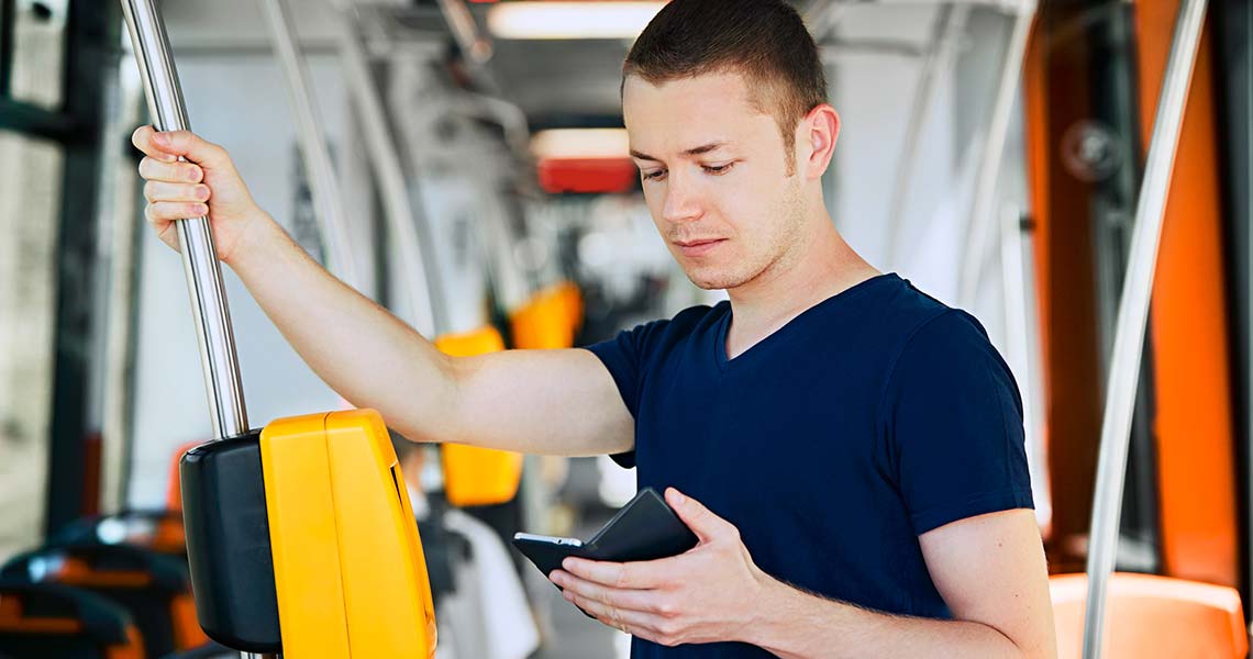 Man sitter vi ett fönster med telefon i handen 