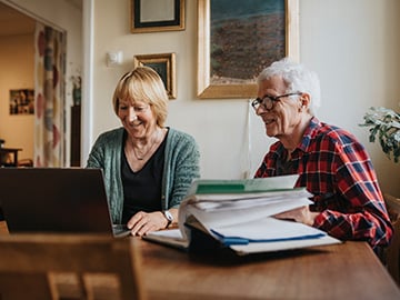 Äldre kvinna och man använder laptop och ler
